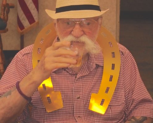 man in fedora drinking with horseshoe cutout around neck